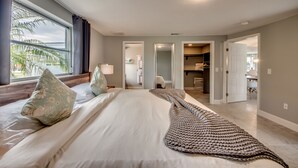 A bedroom with a large bed, a view of the outdoors, and a bathroom visible through an open door. - Villa Seafan - remodeld, new furniture, heated pool, kayaks, perfect for boaters (North Fort Myers)
