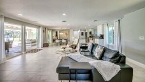 A spacious living area with a black leather sofa, a glass coffee table, and a dining area with chairs and a table. - Villa Seafan - remodeld, new furniture, heated pool, kayaks, perfect for boaters (North Fort Myers)