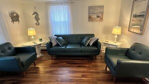 Een woonkamer met een groene bank, twee fauteuils, een bijzettafeltje en een open haard.