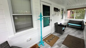 Een veranda met een bankje, een deur met een bord en een welkomstmat.
