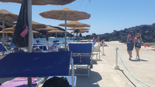 A beach with sun loungers, umbrellas, and a rope barrier.