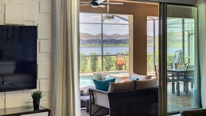 Un salon moderne doté d’un grand téléviseur, d’une porte vitrée donnant sur une terrasse avec mobilier d’extérieur et offrant une vue sur la piscine.