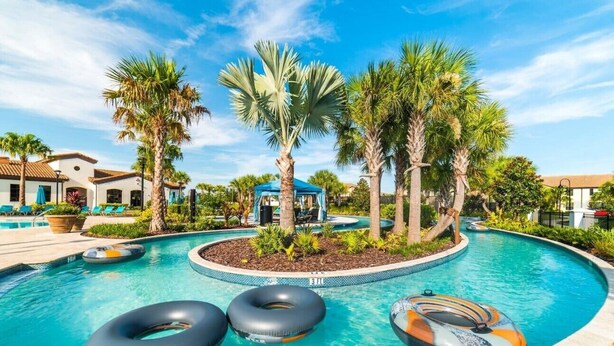 Une piscine avec trois bouées gonflables, des palmiers et des chaises longues.