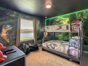 A room with a bunk bed, a dinosaur mural, and a 'Jurassic Park' themed poster.
