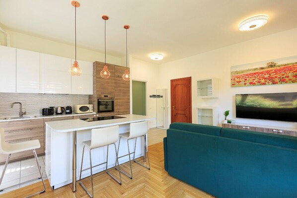 Una cocina moderna con armarios blancos, una isla central con taburetes de bar, iluminación colgante y un televisor de pantalla plana grande montado sobre la isla.