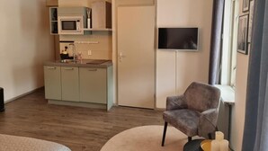 A compact living space with a kitchenette, a flat-screen TV mounted on the wall, a grey armchair, and a small round rug. - Studio Trenz for two - Groningen Center (Groningen)