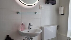 A bathroom with a round mirror, a sink, a toilet, and a towel rack with folded towels. - Studio Trenz for two - Groningen Center (Groningen)