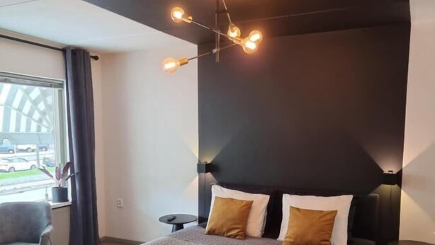 A modern bedroom with a large bed, a dark accent wall, and a ceiling light fixture. - Studio Trenz for two - Groningen Center (Groningen)