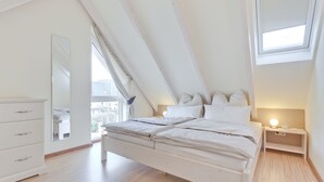 A bedroom with a sloped ceiling, a bed with white bedding, a bedside table with a lamp, and a dresser. - Great vacation home with garden, terrace, 500m to the beach, free WLAN, parking lot (Zingst)