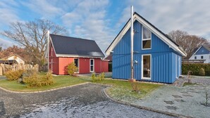 A residential area with two houses, one red and one blue, with a gravel driveway and a grassy lawn. - Great vacation home with garden, terrace, 500m to the beach, free WLAN, parking lot (Zingst)