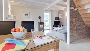 A modern living room with a fireplace, a dining area with a bowl of fruit, and a staircase leading to an upper level. - Great vacation home with garden, terrace, 500m to the beach, free WLAN, parking lot (Zingst)