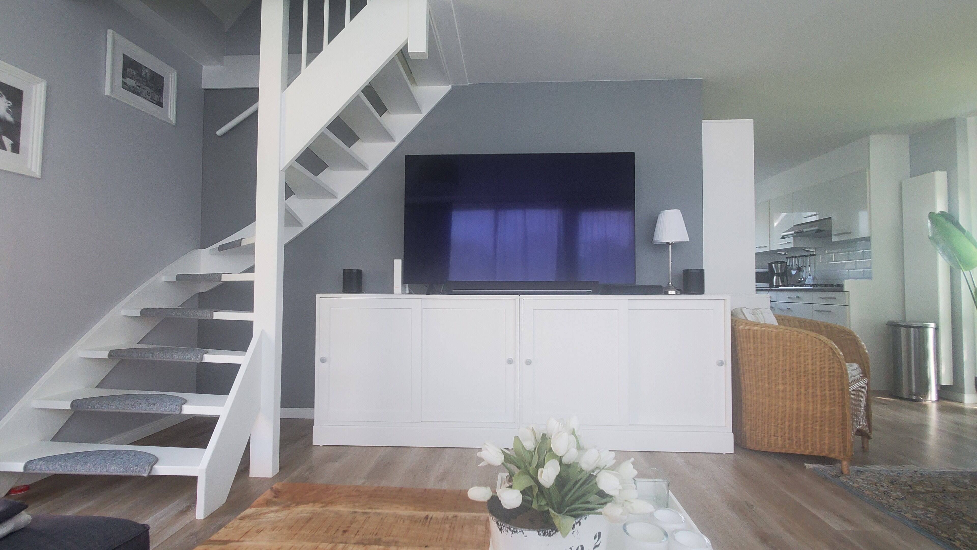Een moderne woonkamer met een trap, een flatscreen televisie, een eethoek en een keuken op de achtergrond.