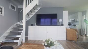 Een moderne woonkamer met een trap, een flatscreen televisie, een eethoek en een keuken op de achtergrond.