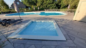 A swimming pool with a small deck area, surrounded by lounge chairs and umbrellas.