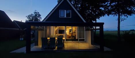 Una casa moderna con fachada de vidrio, un comedor con sillas y una mesa, y una cocina a la vista.
