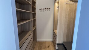 A walk-in closet with wooden shelves and a hanging rod, featuring a light-colored floor and white walls. - Large villa with swimming pool on the outskirts of Bordeaux (BRUGES)