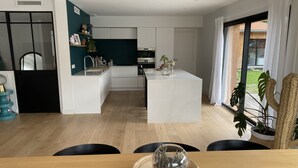 A modern kitchen with white cabinets, a central island, and a dining area with a wooden table. - Large villa with swimming pool on the outskirts of Bordeaux (BRUGES)