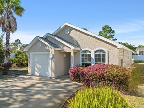 A single-story house with a garage, a covered patio, and a well-maintained garden with flowering shrubs. - Good Vibes PCB- Private and Serene Getaway (Panama City Beach)