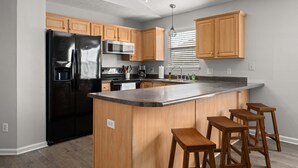 Una cocina moderna con armarios de madera, un refrigerador negro, un microondas y una encimera de granito.