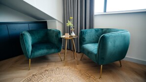 A room with two teal velvet armchairs, a small round table with a vase, and a woven rug on a wooden floor. - MyHotelSteenwijk (Steenwijk)