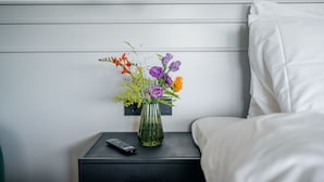 A neatly made bed with white linens, a small bedside table with a remote control, and a vase with flowers. - MyHotelSteenwijk (Steenwijk)