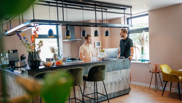 A modern kitchen with a bar area, two bar stools, and a yellow chair. - MyHotelSteenwijk (Steenwijk)