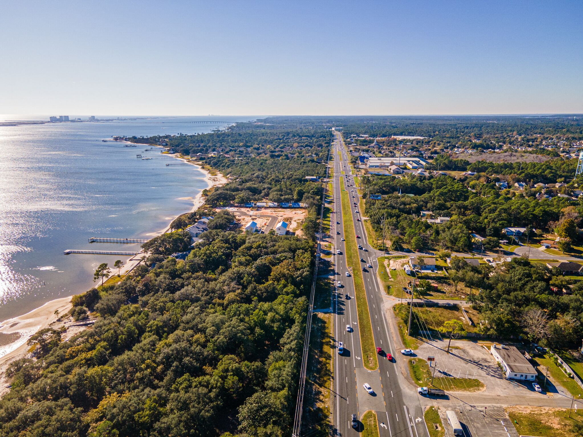 An aerial view of a coastal road with a bridge, beach, and residential areas.