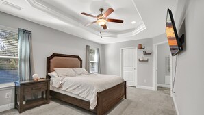 Ein Schlafzimmer mit Bett, Nachttisch, Deckenventilator und einem an der Wand montierten Fernseher.