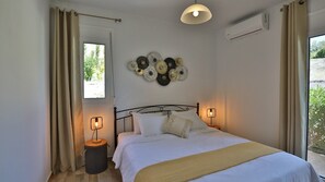 Quarto com cama, duas luminárias de cabeceira, um adorno na parede e uma janela com cortinas.