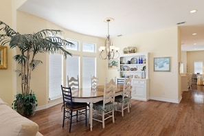 A dining area with a wooden table, white chairs, a chandelier, and a large potted plant.