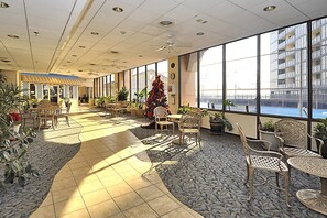 Un vaste espace intérieur doté d’un haut plafond, de grandes fenêtres et de différents types de sièges, notamment des chaises et des tables.