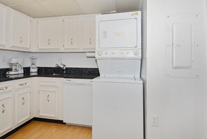 Une cuisine compacte avec des meubles blancs, une machine à café, un mixeur et un réfrigérateur.