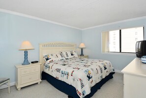 Een slaapkamer met een bed, twee nachtkastjes met lampen, een dressoir en een raam met uitzicht op gebouwen.