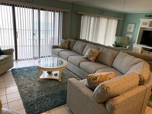A living room with a sofa, a glass coffee table, a rug, and a TV.