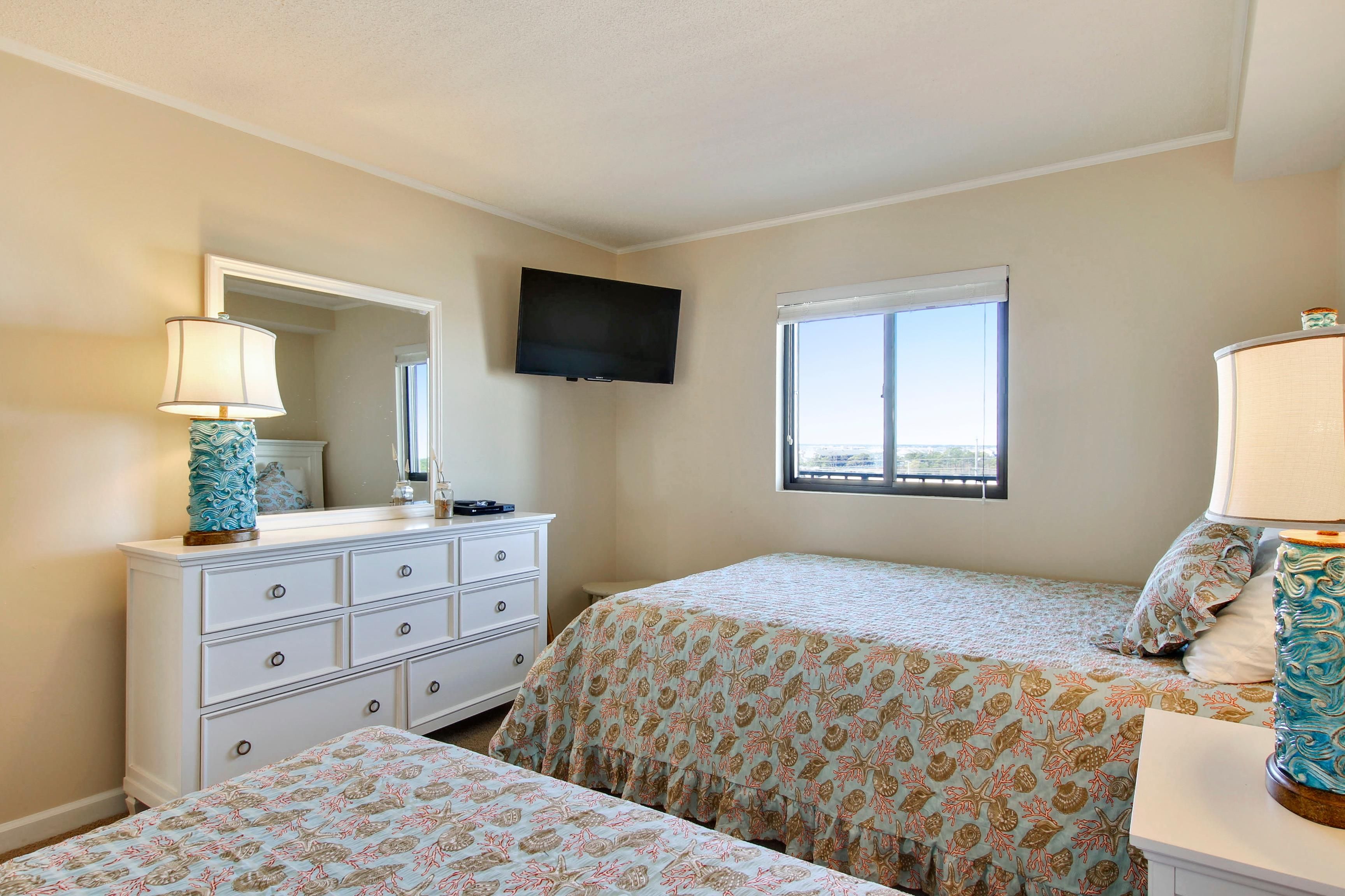 A bedroom with two beds, a dresser, a television, and a window.