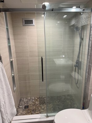 A glass-enclosed shower with a tiled floor, a visible drain, and a handheld showerhead.