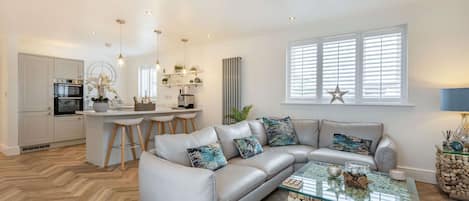 A modern living room with a grey sofa, a glass coffee table, and a herringbone wood floor.