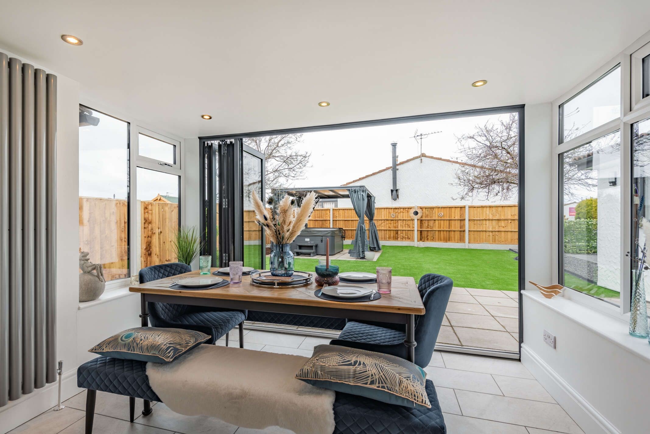 A dining area with a table set for four, large windows, and a view of a backyard.