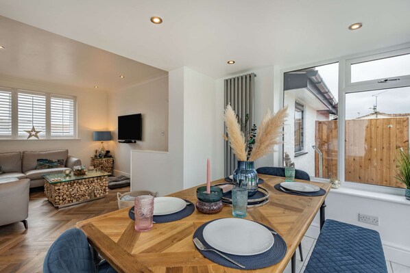 A dining area with a wooden table set for four, surrounded by a modern living space with a sofa, a TV, and a view of the outside. - Tegfan Holiday Home, North Wales With Hot Tub (Abergele)