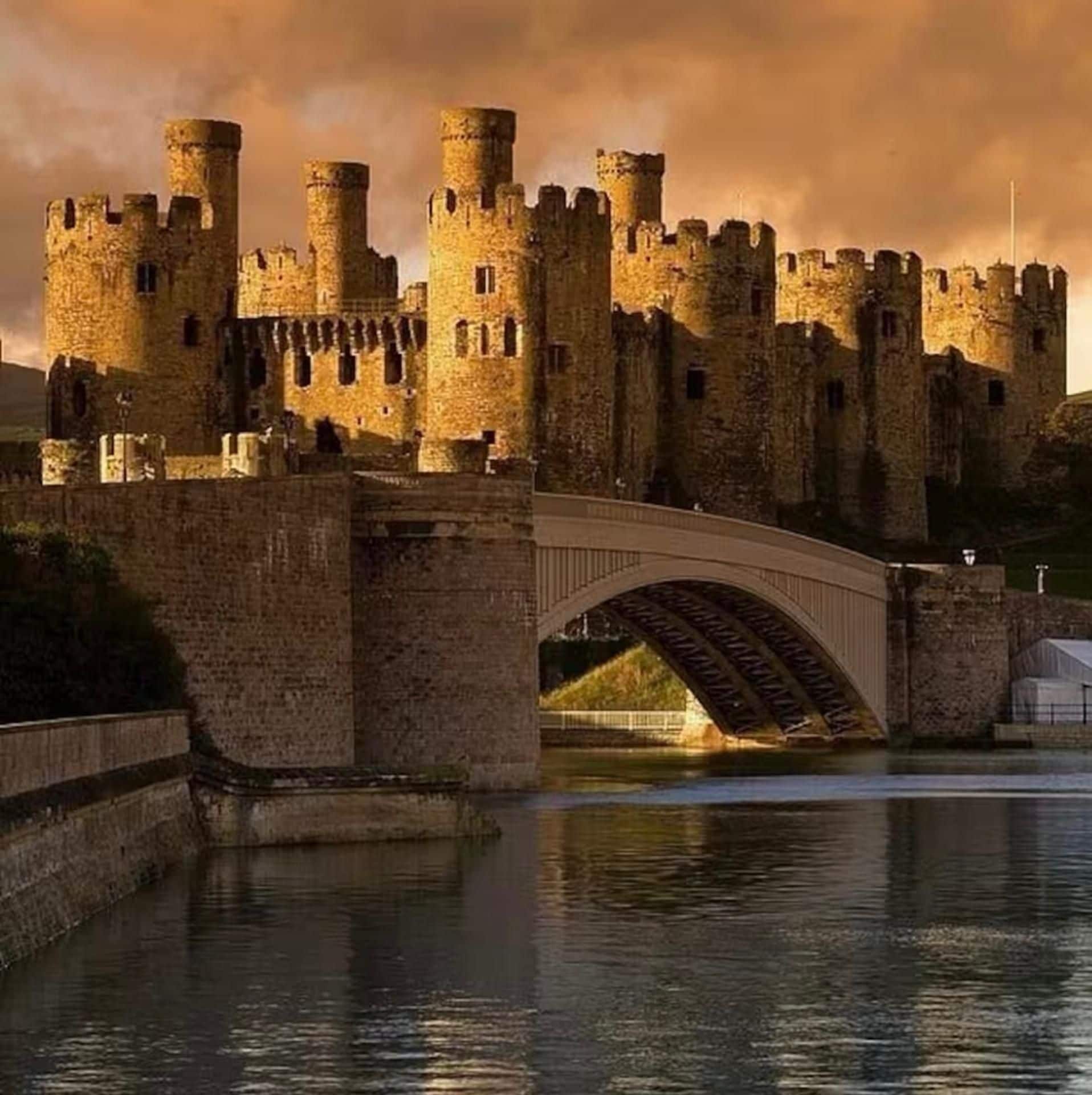 Un château de pierre historique, doté de nombreuses tours et surplombant un plan d’eau par-dessus lequel passe un pont.