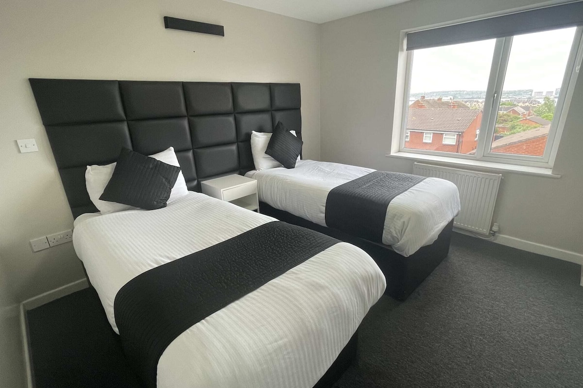 A hotel room with two beds, a large window, and a view of buildings outside.