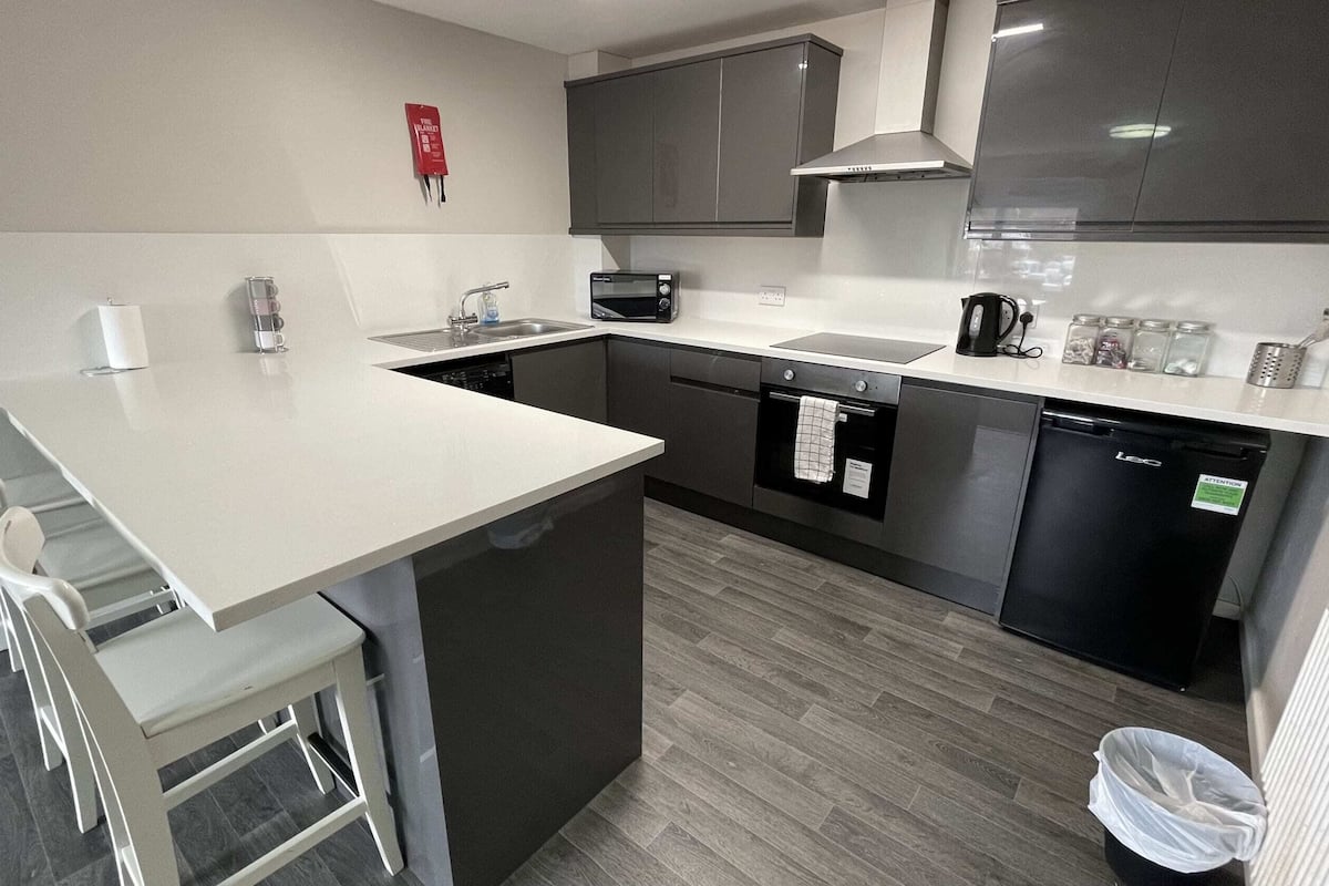 A compact kitchen with a white countertop, dark cabinetry, a built-in oven, and a dishwasher.