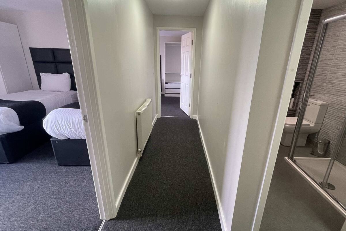 A narrow hallway with a bed on the left, a radiator, and a shower area on the right.