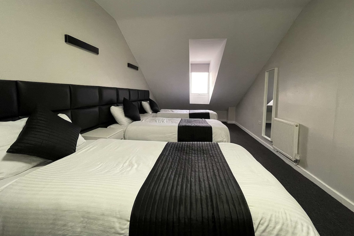 A hotel room with two beds, a black headboard, white bedding, a black accent pillow, a window with a view, and a radiator.