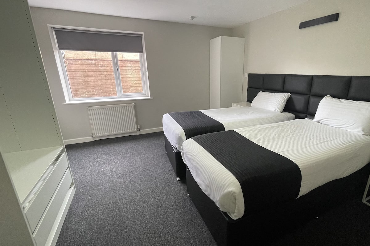 A hotel room with two beds, a radiator, a window, and a white wardrobe.