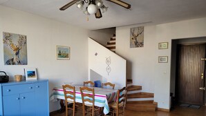 Un coin repas avec une table dressée pour quatre personnes, entourée de chaises en bois. Un meuble bleu se trouve à gauche, et une chaise en osier est placée au premier plan.