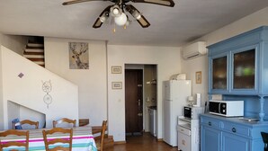 Une cuisine avec un coin repas, des chaises en bois, une nappe à rayures, un ventilateur de plafond et un meuble bleu.