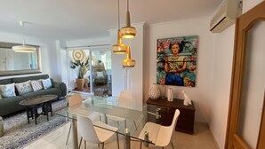 A modern living room with a glass dining table, white chairs, a sofa, and a large painting on the wall. - Penthouse Javea 100 meters  from the beach (Xàbia)