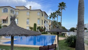 A swimming pool with a bench, surrounded by palm trees and a building with balconies. - Penthouse Javea 100 meters  from the beach (Xàbia)