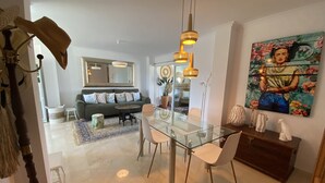 A modern living room with a glass dining table, a sofa, and a large painting. - Penthouse Javea 100 meters  from the beach (Xàbia)